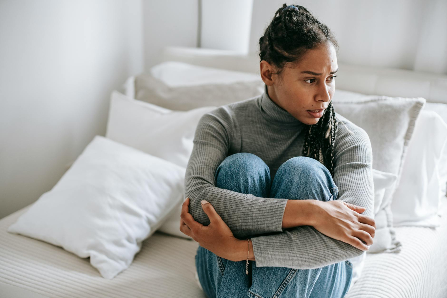A worried woman sitting on a bed with her arms wrapped around her knees