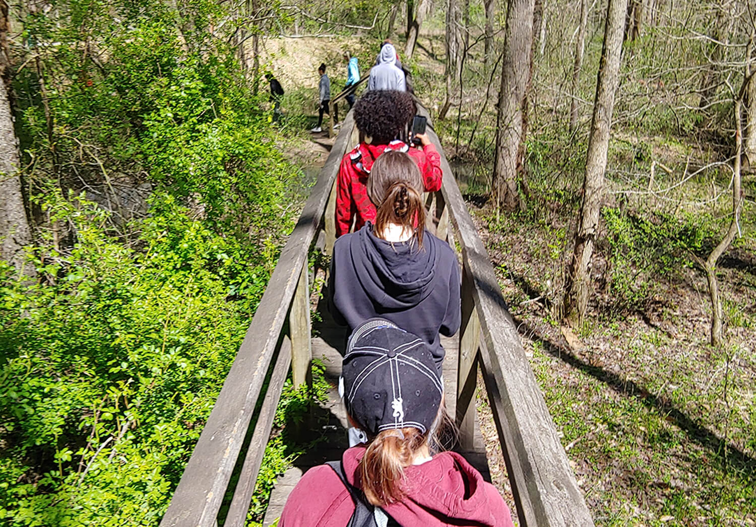 A group of young people in a program crossing a narrow wooden bridge.