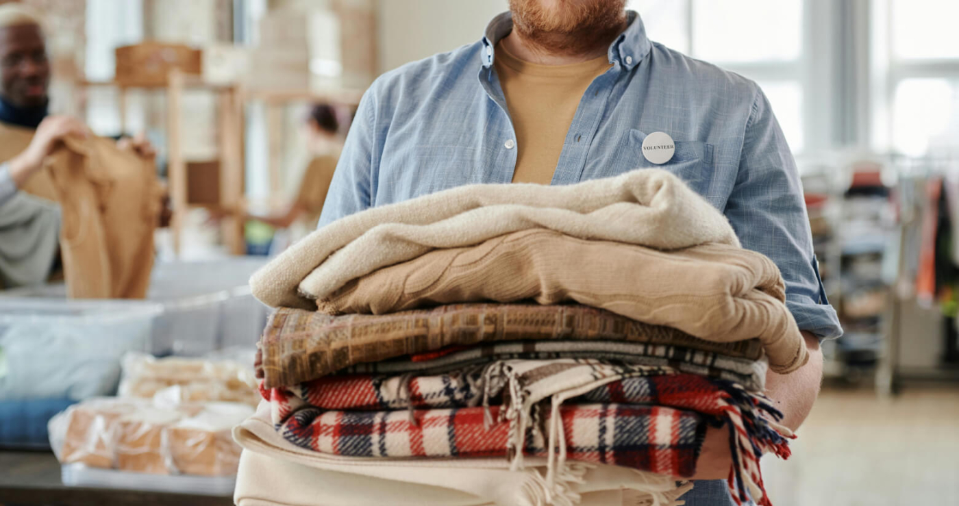 A volunteer holds a stack of donated warm clothes and blankets in a community donation center